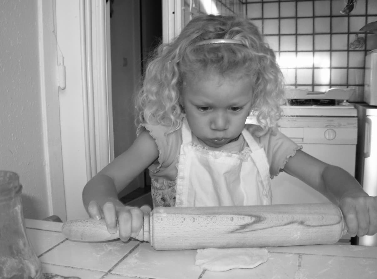 Théa, petite fille, en train de pétrir avec un rouleau à pâtisserie